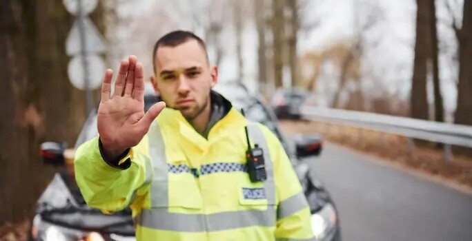 Foto-policial-masculino-de-uniforme-verde-mostrando-o-gesto-de-parada-perto-do-veiculo